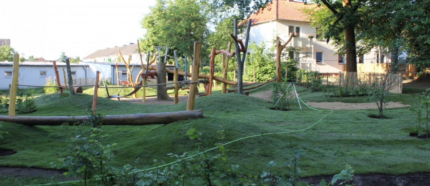 Spielplatz mit Spielgeräten für draußen in einer hügeligen grünen Parkanlage.